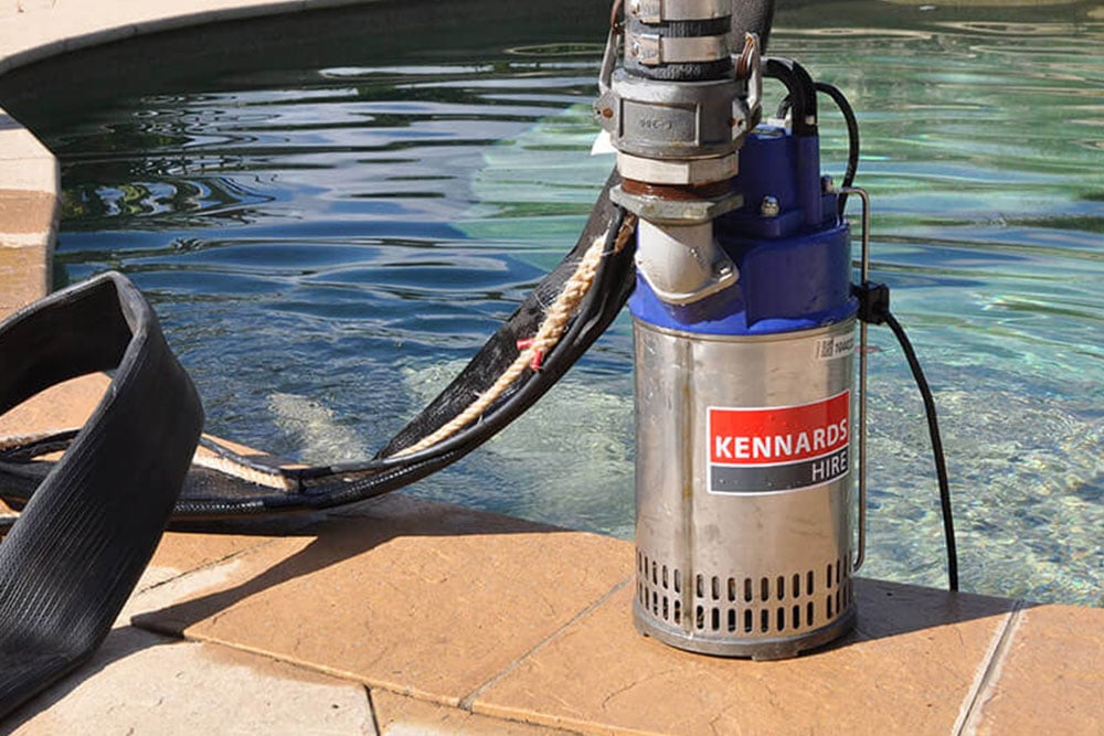  A submersible pump with the Kennards Hire logo placed on the edge of a swimming pool, ready for use.
