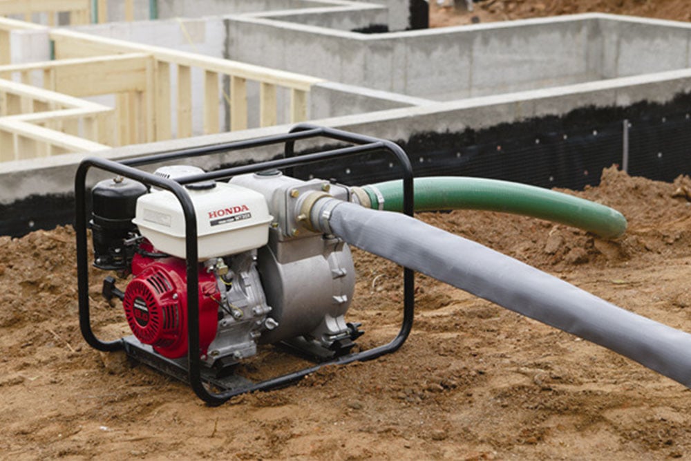 A small pump with the Kennards Hire logo sitting on dirt at a construction work site