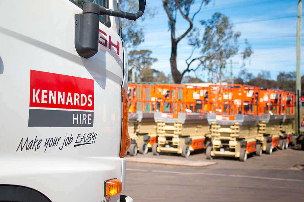 A Kennards Hire truck in the foreground. A background of parked boom lifts