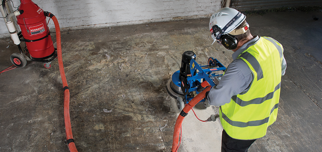 Kennards Hire team member operating a concrete grinder on a warehouse floor while wearing high-visibility safety gear and protective equipment.