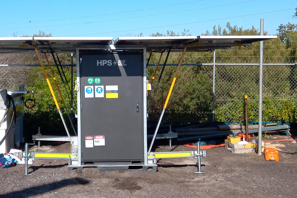 Portable solar-powered renewable energy system with fold-out solar panels, situated outdoors near a fenced area